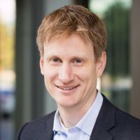 Portrait of a smiling researcher in a suit, likely involved in cancer research.